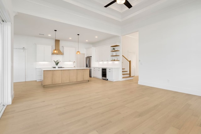 kitchen featuring white cabinets, light hardwood / wood-style floors, wall chimney range hood, and a large island