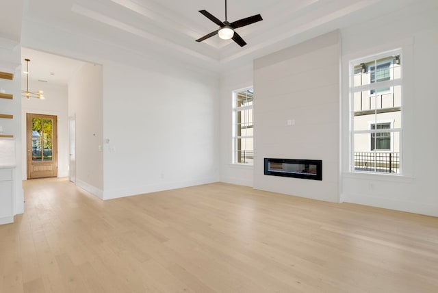 unfurnished living room featuring a fireplace, a towering ceiling, light hardwood / wood-style flooring, a tray ceiling, and ceiling fan with notable chandelier