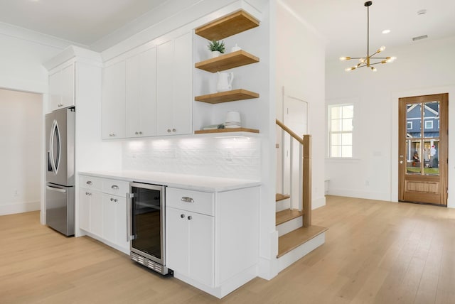 kitchen featuring white cabinets, decorative backsplash, stainless steel refrigerator, light wood-type flooring, and wine cooler