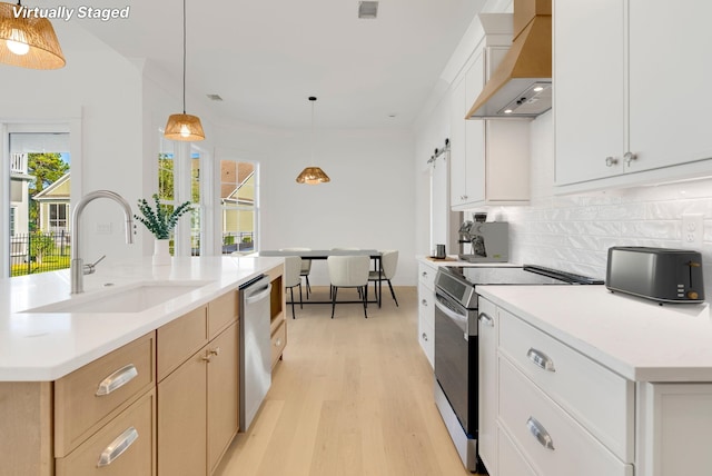 kitchen with pendant lighting, appliances with stainless steel finishes, white cabinetry, and wall chimney range hood