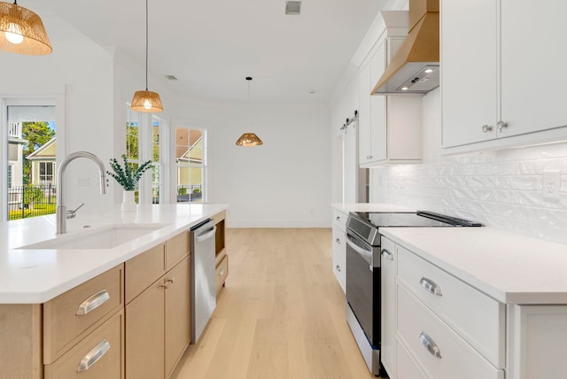 kitchen featuring wall chimney range hood, appliances with stainless steel finishes, decorative light fixtures, and white cabinets