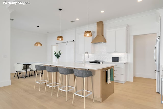 kitchen with decorative light fixtures, white cabinetry, premium range hood, and a center island with sink