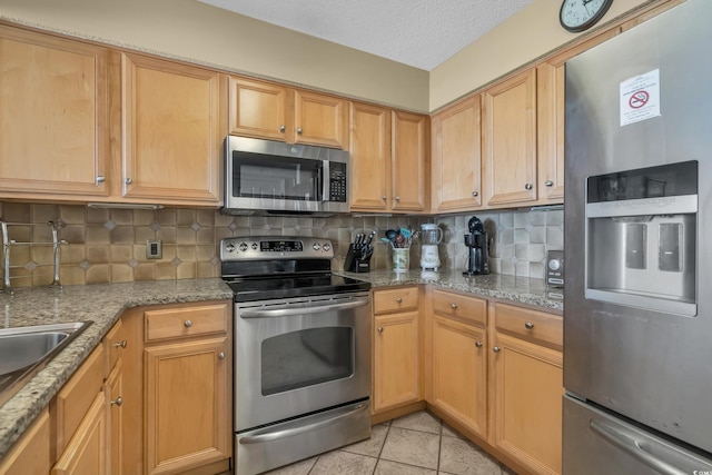 kitchen featuring light stone counters, a textured ceiling, light tile patterned floors, backsplash, and appliances with stainless steel finishes