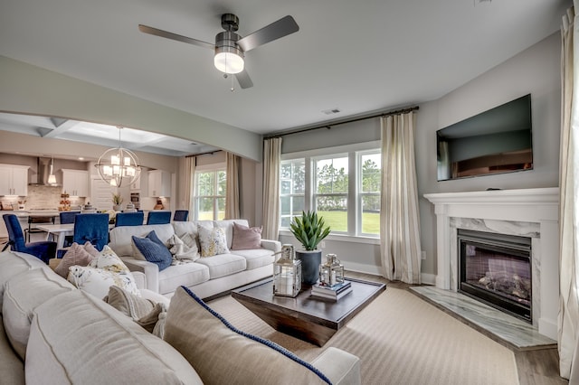 living room with light wood-type flooring, a high end fireplace, beam ceiling, and ceiling fan with notable chandelier