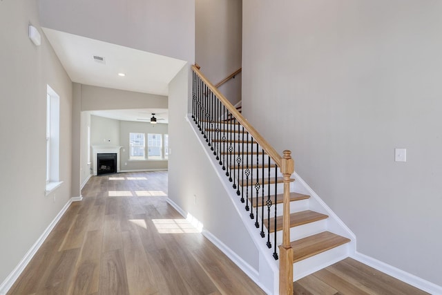 staircase with hardwood / wood-style floors, ceiling fan, and high vaulted ceiling