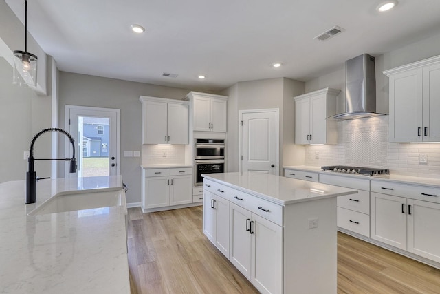 kitchen featuring appliances with stainless steel finishes, decorative light fixtures, light hardwood / wood-style flooring, white cabinets, and wall chimney range hood