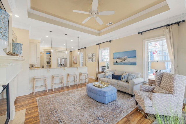 living room featuring crown molding, a tray ceiling, and light hardwood / wood-style floors