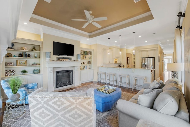 living room with built in features, ornamental molding, a tray ceiling, and light wood-type flooring