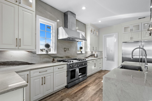 kitchen with wall chimney exhaust hood, decorative light fixtures, hardwood / wood-style floors, range with two ovens, and white cabinets