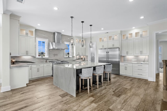 kitchen with premium appliances, white cabinetry, wall chimney range hood, and light hardwood / wood-style flooring