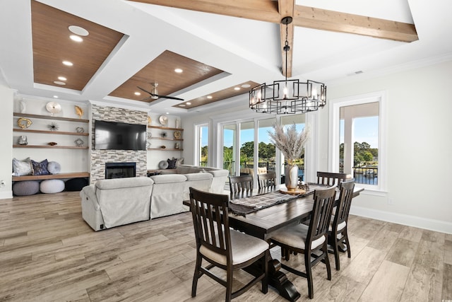 dining space featuring built in shelves, ceiling fan with notable chandelier, beam ceiling, a fireplace, and light hardwood / wood-style flooring