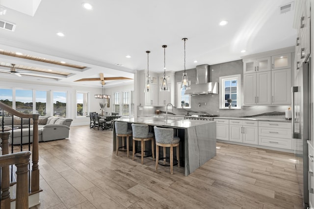 kitchen with white cabinets, light wood-type flooring, wall chimney exhaust hood, and a kitchen island with sink