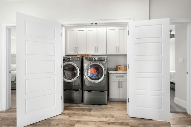 laundry area with cabinets, light hardwood / wood-style flooring, and washing machine and clothes dryer