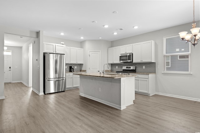 kitchen featuring white cabinets, light wood-type flooring, stainless steel appliances, and a center island with sink