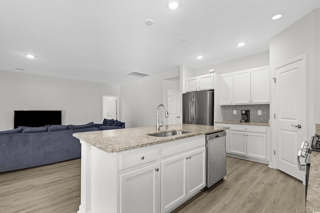 kitchen featuring stainless steel appliances, white cabinetry, sink, an island with sink, and light hardwood / wood-style flooring