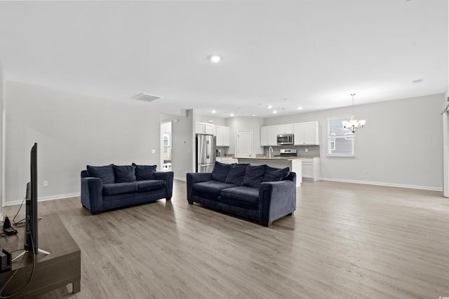 living room with a chandelier, sink, and light wood-type flooring