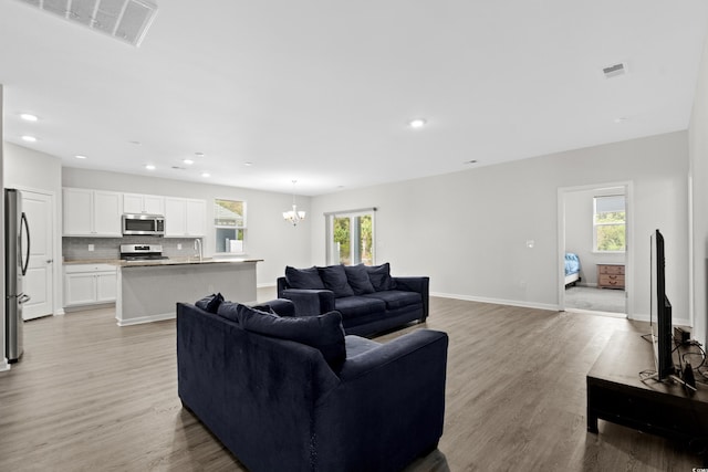 living room featuring plenty of natural light, light hardwood / wood-style floors, sink, and an inviting chandelier