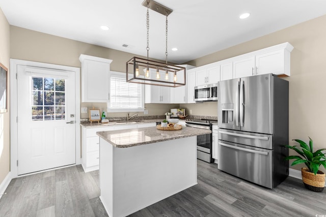 kitchen with white cabinets, appliances with stainless steel finishes, decorative light fixtures, and a center island