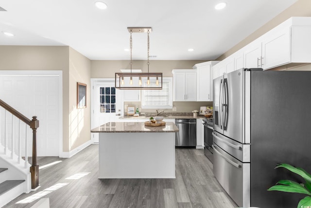 kitchen featuring stainless steel appliances, white cabinetry, dark stone counters, hardwood / wood-style floors, and a kitchen island