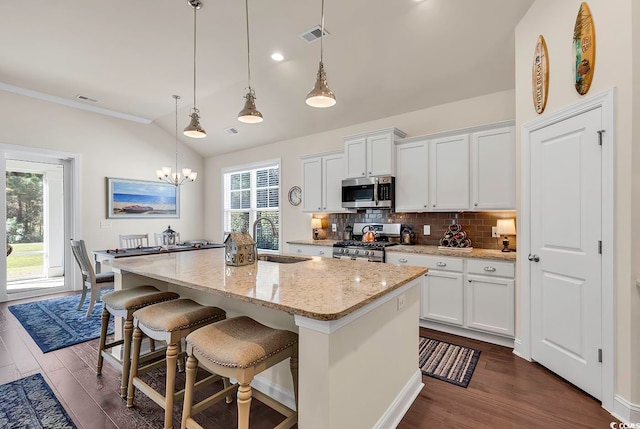 kitchen with stainless steel appliances, white cabinetry, sink, decorative light fixtures, and a kitchen island with sink