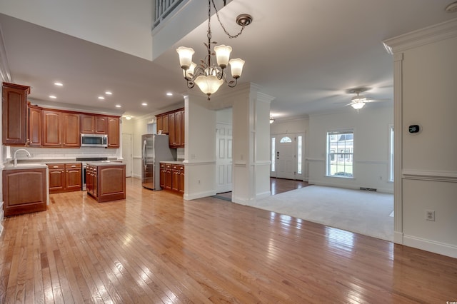 kitchen featuring appliances with stainless steel finishes, a kitchen island, pendant lighting, ornamental molding, and light wood-type flooring