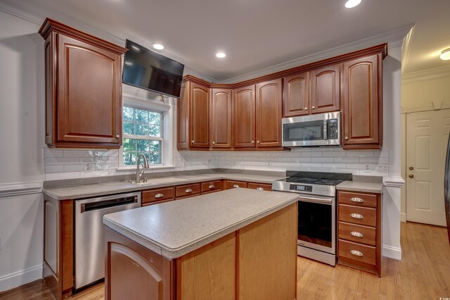 kitchen with sink, appliances with stainless steel finishes, light hardwood / wood-style flooring, crown molding, and a kitchen island