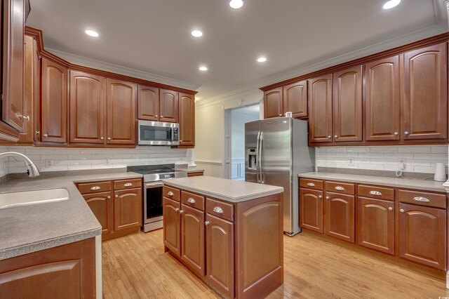 kitchen featuring ornamental molding, stainless steel appliances, a kitchen island, sink, and light hardwood / wood-style floors