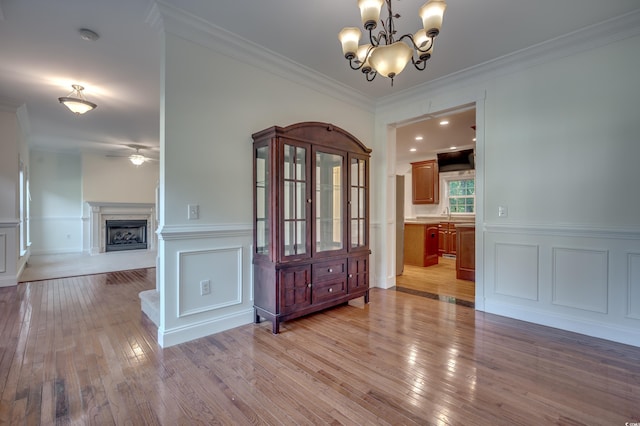 unfurnished dining area featuring ceiling fan with notable chandelier, crown molding, and light hardwood / wood-style flooring