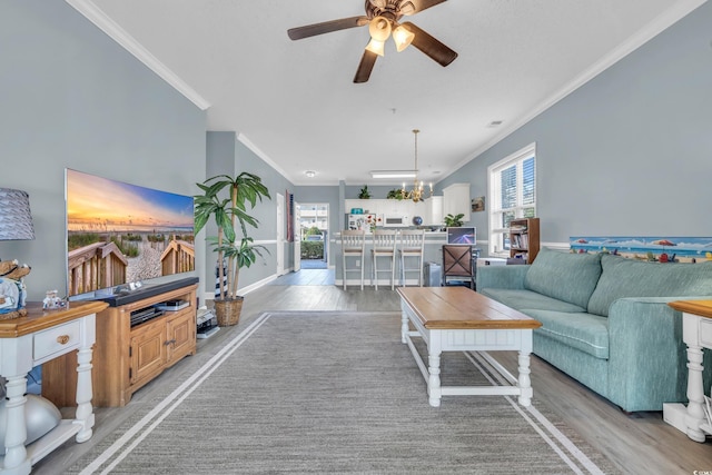 living room with ceiling fan with notable chandelier, crown molding, and light hardwood / wood-style flooring