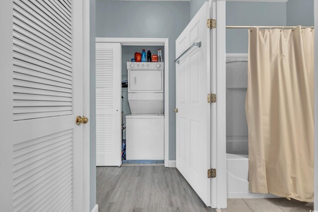 laundry area with light wood-type flooring and stacked washer / dryer