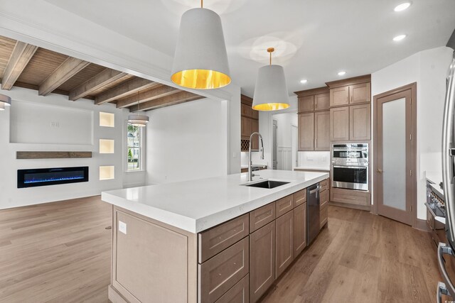 kitchen with stainless steel appliances, sink, pendant lighting, beamed ceiling, and an island with sink