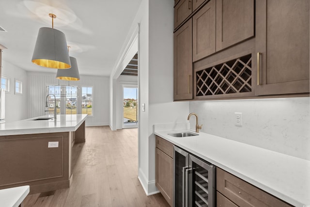 kitchen with sink, hanging light fixtures, beverage cooler, and light hardwood / wood-style flooring