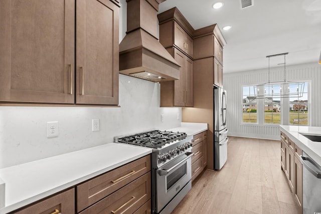 kitchen with premium range hood, decorative light fixtures, light hardwood / wood-style floors, stainless steel appliances, and a chandelier