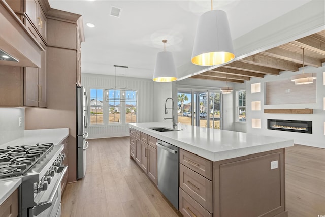 kitchen with a center island with sink, sink, stainless steel appliances, and hanging light fixtures