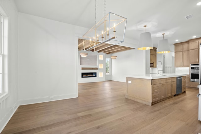 kitchen featuring beamed ceiling, light hardwood / wood-style floors, decorative light fixtures, a fireplace, and a center island with sink