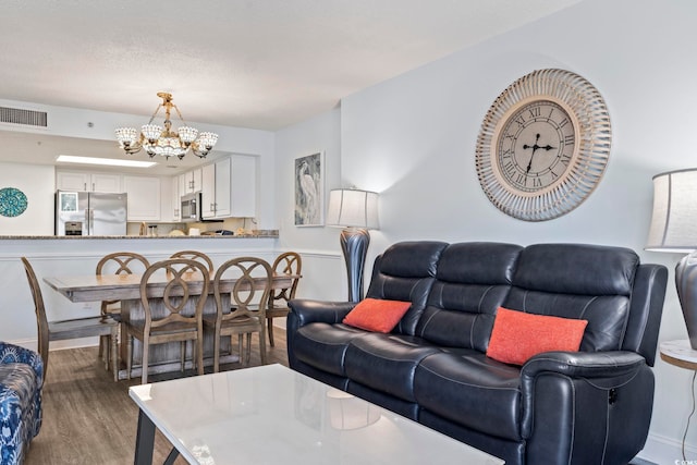 living area with visible vents, wood finished floors, baseboards, and a notable chandelier