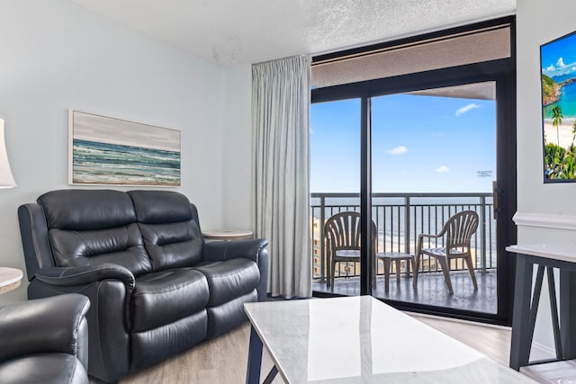 living room featuring a water view, a textured ceiling, light hardwood / wood-style flooring, and floor to ceiling windows