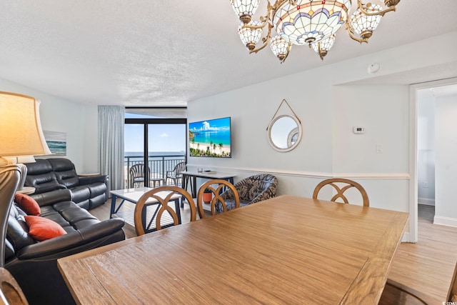 dining area with a textured ceiling, hardwood / wood-style floors, an inviting chandelier, and a wall of windows