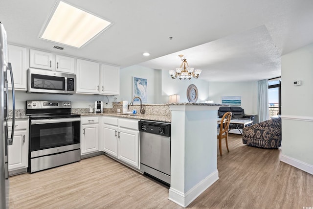 kitchen featuring light wood finished floors, stainless steel appliances, a peninsula, and a sink