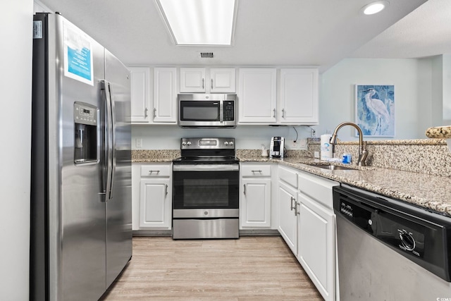 kitchen with stainless steel appliances, light stone counters, sink, white cabinetry, and light wood-type flooring