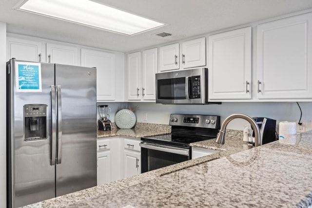 kitchen with white cabinetry, light stone countertops, appliances with stainless steel finishes, and visible vents