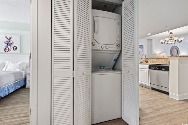 laundry area featuring stacked washer and clothes dryer, a chandelier, sink, and light hardwood / wood-style flooring