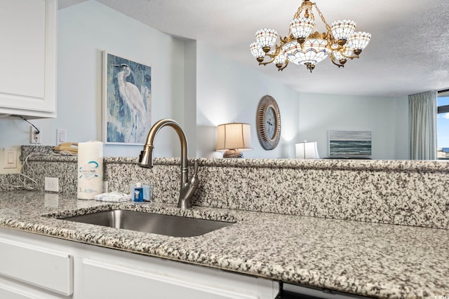 kitchen with white cabinetry, sink, light stone counters, a textured ceiling, and decorative light fixtures