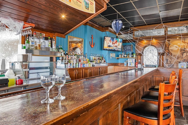 bar with a dry bar, ornamental molding, and wood walls