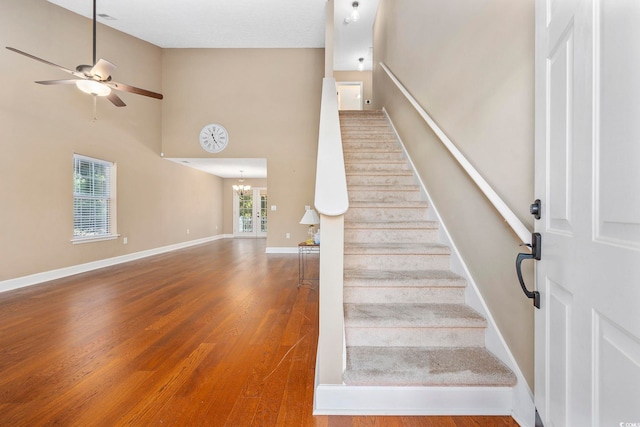 stairs featuring ceiling fan with notable chandelier, hardwood / wood-style flooring, and a high ceiling