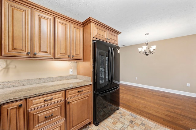 kitchen featuring light stone counters, pendant lighting, an inviting chandelier, black refrigerator, and light wood-type flooring