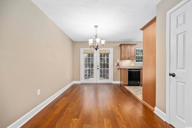 unfurnished living room with french doors, a chandelier, a textured ceiling, and dark hardwood / wood-style flooring