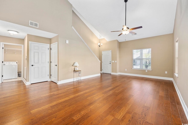 unfurnished living room featuring a towering ceiling, hardwood / wood-style flooring, ceiling fan, and washer / dryer