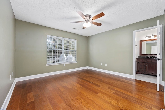 unfurnished bedroom featuring hardwood / wood-style floors, a textured ceiling, ceiling fan, and connected bathroom