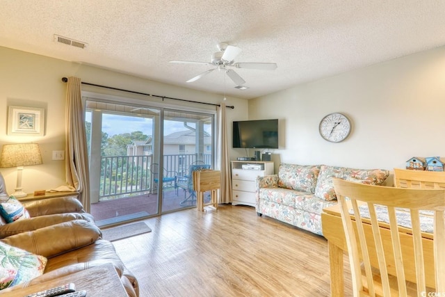 living room with ceiling fan, a textured ceiling, and light wood-type flooring